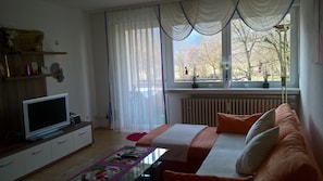 Ein Schlafzimmer mit einem Bett, einem Fernseher, einem Schminktisch und einem Fenster mit Vorhängen.