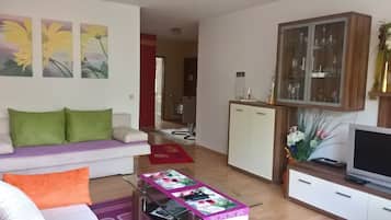 Ein Wohnzimmer mit einer Couch, einem Couchtisch mit Zeitschriften, einem Fernseher und einer Vitrine.