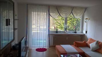 Ein Zimmer mit einem Bett, einem Heizkörper, einem Fenster mit Vorhängen, einer Zimmerpflanze und einer Lampe.