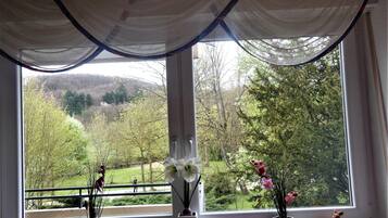 Ein Fenster mit Blick auf eine bewaldete Landschaft, ein kleiner Tisch mit Dekoration und ein Vorhang.