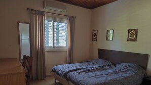 Une chambre à coucher comprenant un lit, un bureau, une chaise, une fenêtre avec des rideaux et un climatiseur fixé au mur.