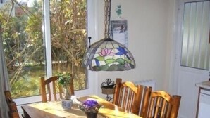 Un coin repas avec une table en bois, des chaises, un luminaire en vitrail et une vue sur la verdure à l’extérieur.