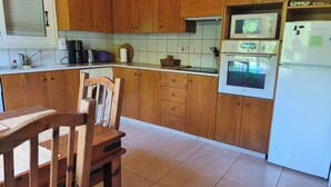 A kitchen with wooden cabinets, a washing machine, a microwave, and a refrigerator. - Rural apartment in Cyprus (Psevdas)