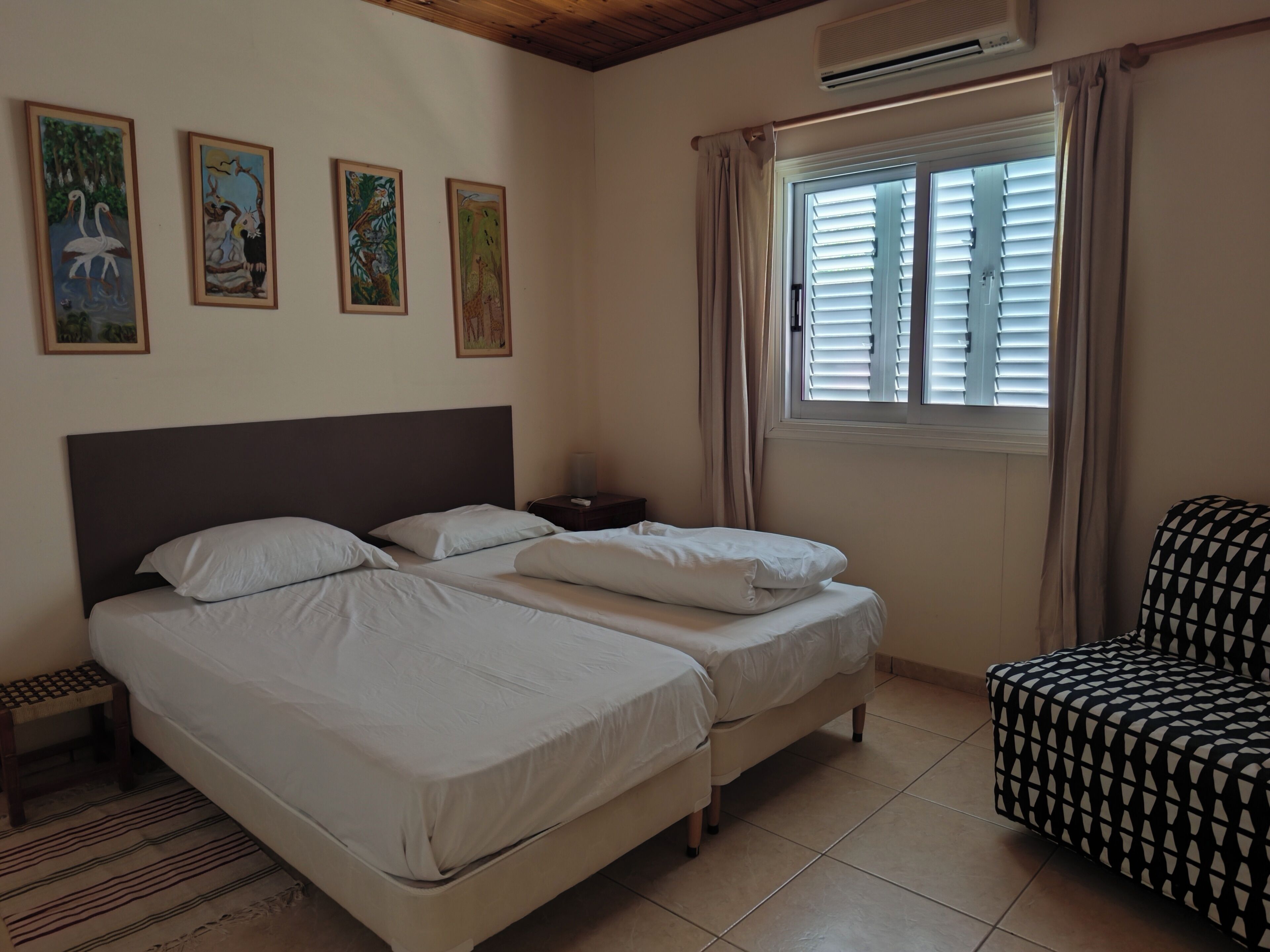A hotel room with two beds, a chair, a nightstand, and wall art.