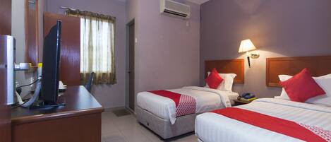 A hotel room with two beds, a desk, a television, and an air conditioning unit.