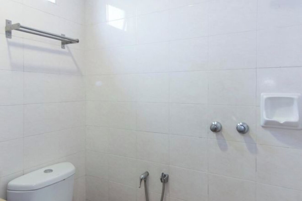 A bathroom with white tiles, a toilet, a handrail, and a soap dispenser.