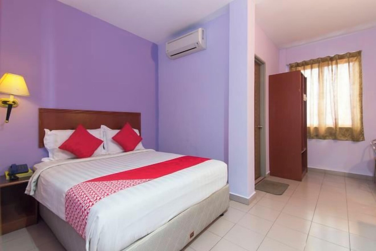 Habitación de hotel con cama, mesita de noche, equipo de aire acondicionado y ventana con cortinas.