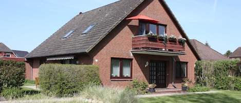 Une maison à deux étages, construite en briques, avec un toit en pente, un balcon agrémenté de plantes en pot et une pelouse bien entretenue.