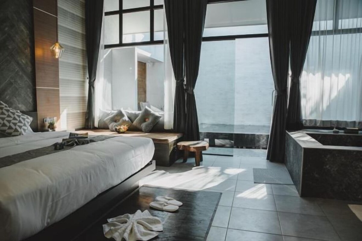 Un hotel moderno con una cama grande, una mesita, zona de estar, bañera y vistas al mar.
