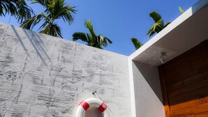 A white textured wall with a lifebuoy hanging on it and palm trees in the background. - Arun Dara Villa (Chiang Mai)