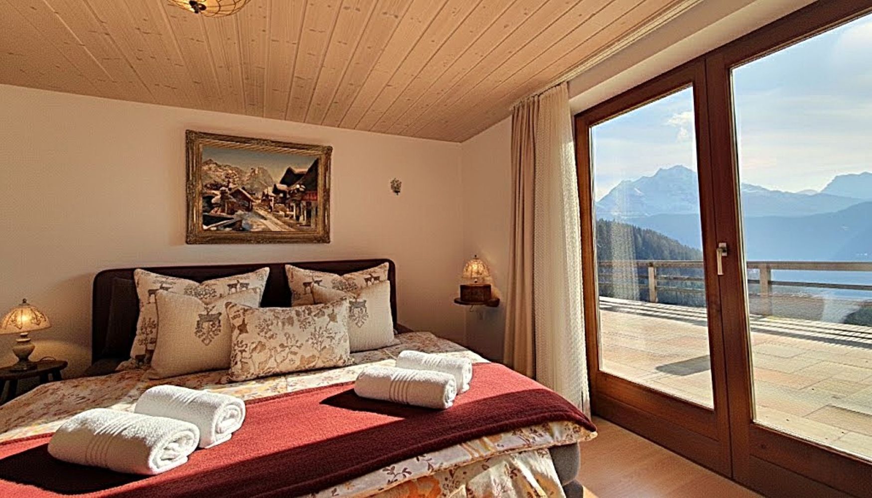 Une chambre à coucher avec un grand lit, un tableau au-dessus du lit et une vue sur les montagnes par une porte vitrée.