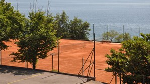 Un court de tennis avec un filet, entouré d’arbres et offrant une vue sur une vaste étendue d’eau.