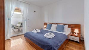 Une chambre à coucher bien aménagée, avec un lit, des tables de chevet et une vue sur un espace extérieur aménagé en salon, visible à travers une porte vitrée.