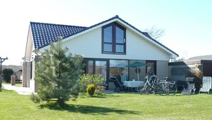 A two-story house with a tiled roof, large windows, and a patio area with outdoor furniture and bicycles.