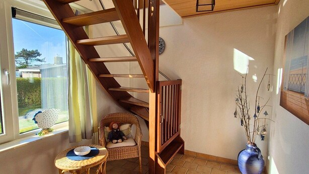 A spacious room with a wooden staircase, a wicker chair, a small table, and a vase with branches.