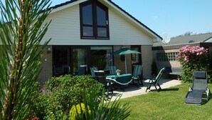 A house with a large window, a patio with chairs and a table, and a lawn.