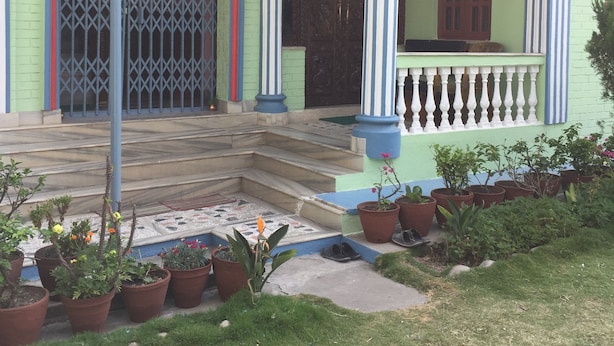 Una casa de dues plantes amb un porxo, escales i plantes en testos.
