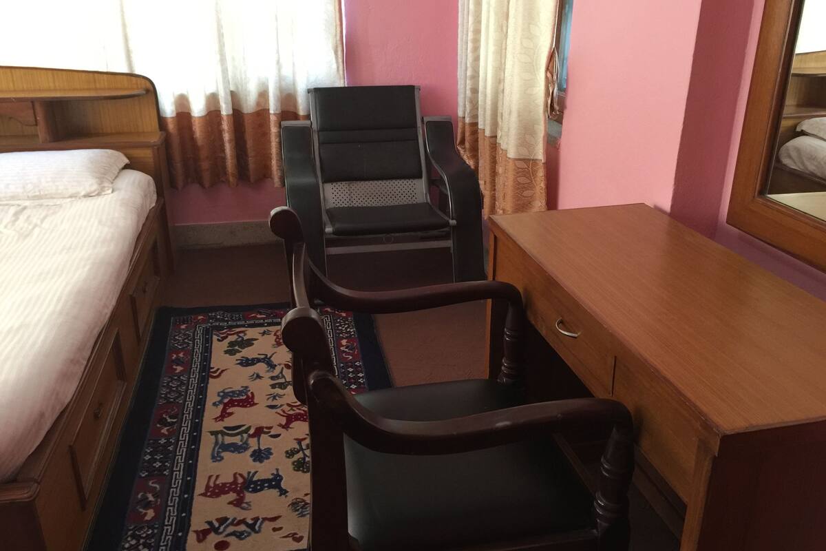 A room with a bed, a desk, two chairs, a rug, and a mirror.