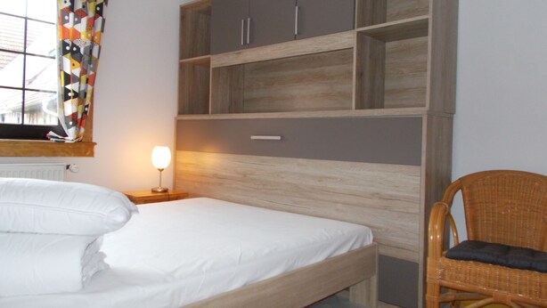 Ein Schlafzimmer mit einem Bett, einem Nachttisch mit Lampe, einem Korbstuhl und eingebauten Holzböden.