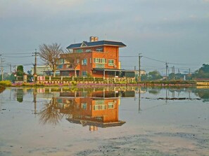 Un edificio a due piani con un balcone, circondato da uno specchio d'acqua che riflette l'edificio.