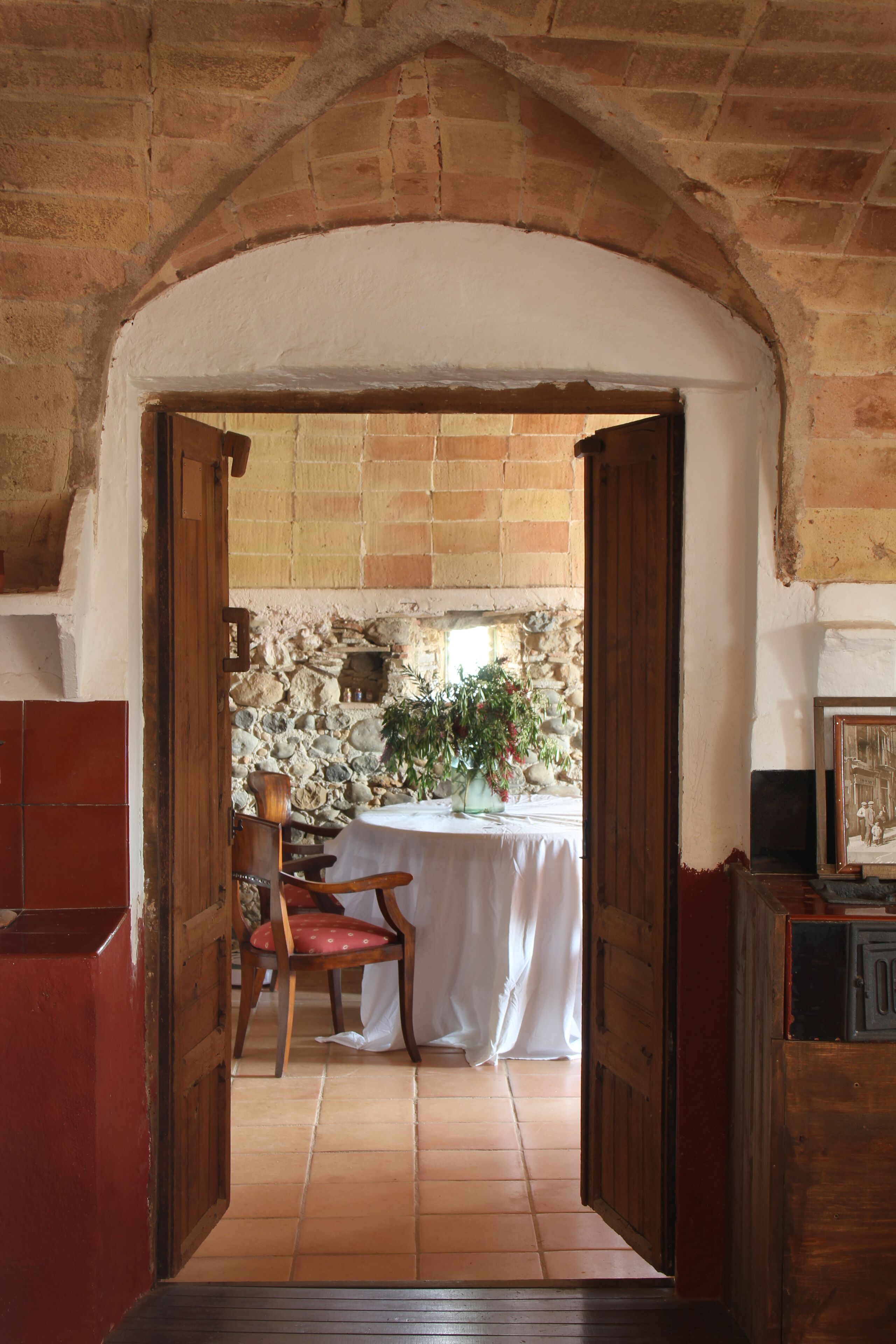 An arched doorway leading to a room with a table set for dining, a chair, and a potted plant.