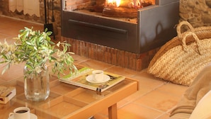 Una habitación de paredes de piedra con chimenea, una mesa de madera con revistas, una taza de café y un bolso tejido.