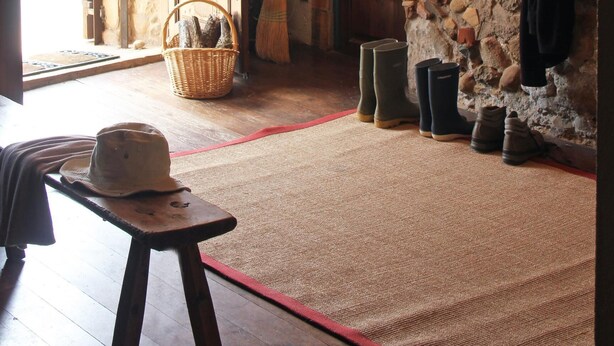 Una habitación rústica con pared de piedra, un banco de madera, un sombrero y botas.