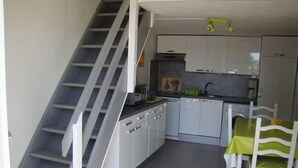 Une cuisine avec des meubles blancs, une table à manger avec des chaises et un escalier.
