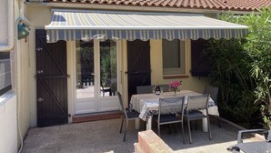 Une terrasse avec une table dressée pour deux personnes, un auvent à rayures et une porte donnant sur un espace extérieur.