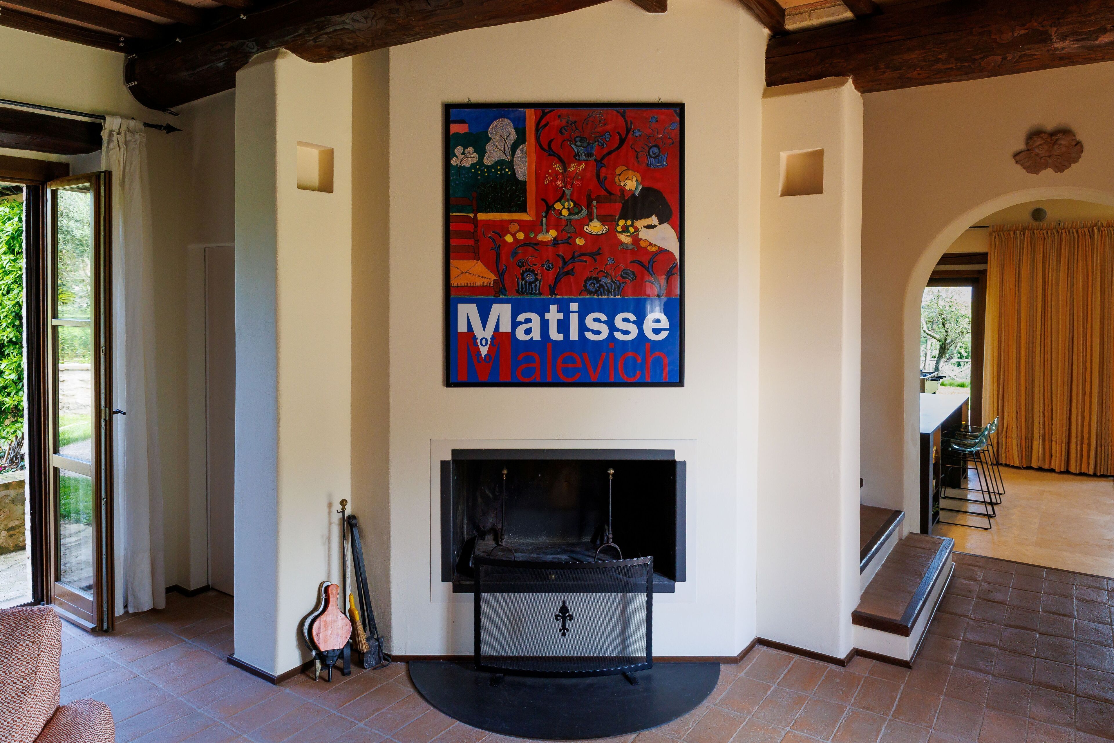A living room with a fireplace, a large abstract painting, and a view of the outdoors.
