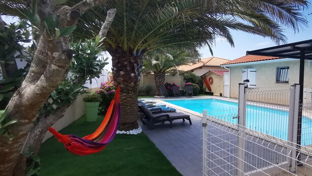 Un patio trasero con piscina, una hamaca y un área cercada con sillones de descanso.