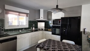 Una cocina con armarios blancos, un refrigerador negro, un microondas y un lavamanos.