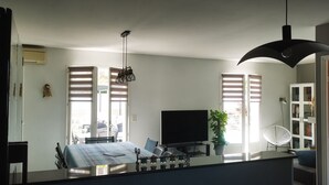 Una cocina moderna con una isla central, un comedor con sillas, un televisor y una planta en maceta.