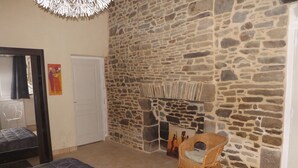 Une chambre avec un mur en pierre, un lit recouvert d’une couette à motifs, une chaise en osier et une porte blanche.
