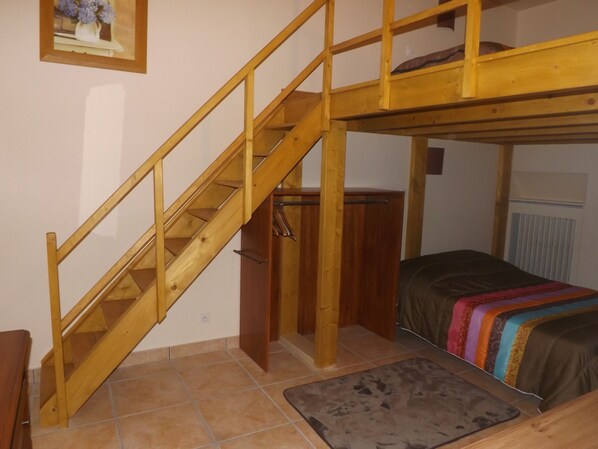 Une chambre avec un lit superposé, un escalier en bois et un petit tapis.