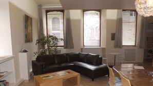 Un salon avec un canapé en cuir noir, une table basse en bois et un coin repas comprenant une table et des chaises en bois.