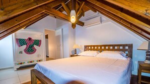 Un dormitorio con una cama de madera, ropa de cama blanca, una mesita de noche con lámpara y un aplique de techo.