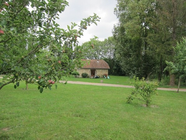 A stone building with a red-tiled roof, surrounded by a grassy area and trees. - Source cottage, this is the little house in the meadow! (Chambly)