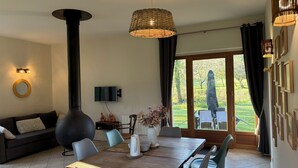 Un comedor con mesa de madera, sillas, televisor y vistas al exterior.