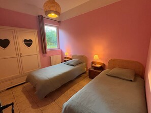 Un dormitorio con dos camas individuales, un armario con detalles en forma de corazón, una ventana con cortinas y una lámpara colgante.