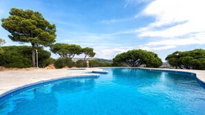 Ein klarer, blauer Swimmingpool mit Stufen, umgeben von Bäumen und wolkenlosem Himmel.