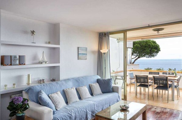 A modern living room with a sofa, coffee table, and a view of the sea through large glass doors.