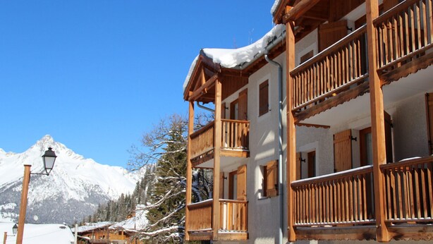 A wooden building with balconies and a mountain in the background. - 4-room apartment, 6-8 people, near ski slopes (Valfréjus)