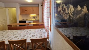 A compact kitchen with wooden cabinets, a stove, and a dining area with a table and chairs. - 4-room apartment, 6-8 people, near ski slopes (Valfréjus)