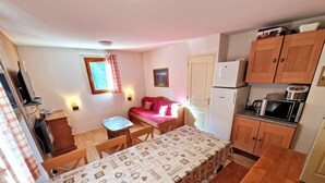 A compact kitchen with a dining table, a small sofa, and wooden cabinets. - 4-room apartment, 6-8 people, near ski slopes (Valfréjus)