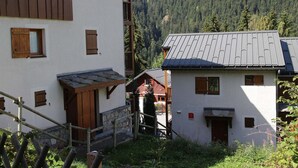 A traditional chalet with a stone staircase, wooden shutters, and a view of a forested valley. - 4-room apartment, 6-8 people, near ski slopes (Valfréjus)