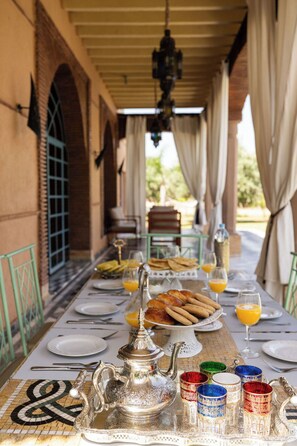 A dining table set with plates, glasses, a teapot, and a tray of pastries.