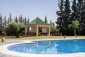A pool with a gazebo, surrounded by trees and a clear sky.