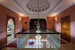 A hotel lobby with a central fountain, a wooden door, and a staircase with ornate railings.