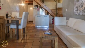 Ein geräumiger Wohnbereich mit einer Holztreppe, einem weißen Sofa, einem Esstisch mit Stühlen und einer Küche im Hintergrund.